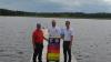Stefan Rampp (rechts) von der AOK Kaufbeuren-Ostallgäu und Benjamin Rößle (Mitte) von der Wasserwacht Marktoberdorf übergeben Betreiber Reinhard Geppert (links) die neue UV-Index-Tafel für das Seebad Elbsee in Aitrang.