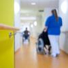 Eine Pflegerin schiebt eine Bewohnerin eines Pflegeheims in einem Rollstuhl über den Flur.