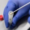 Ein Mann zeigt einen Abstrich für das Testverfahren auf das Virus SARS-CoV-2.