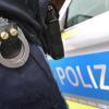 Ein Polizist mit Handschellen und einer Pistole am Gürtel steht vor einem Streifenwagen.