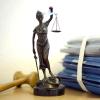 Eine modellhafte Nachbildung der Justitia steht neben einem Holzhammer und einem Aktenstapel.