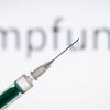 Eine Spritze wird vor den Schriftzug «Impfung» gehalten.