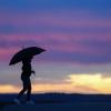 Eine Frau mit Schirm geht am Morgen bei leichtem Nieselregen spazieren. Eine Frau mit Schirm geht am Morgen bei leichtem Nieselregen spazieren.