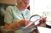Eine sehbehinderte Seniorin liest mit einer Lupe ein Printprodukt. Elderly woman using a magnifier to read a book