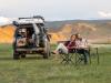 Dilara und Stefan Grebner sitzen neben ihrem ausgebauten Geländewagen an einem Campingtisch, mitten in der endlosen Grassteppe der Mongolei.