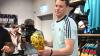 Lächelnd signiert Manuel Neuer einen goldenen WM-Pokal.