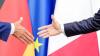 Bundeskanzler Friedrich Merz und Frankreichs Präsident Emmanuel Macron reichen sich die Hände. Die Politiker Christoph Heusgen und Brund Le Maire appelieren an eine viel weitreichendere deutsch-französische Zusammenarbeit.