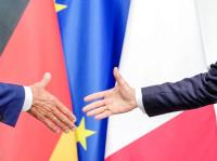Bundeskanzler Friedrich Merz und Frankreichs Präsident Emmanuel Macron reichen sich die Hände. Die Politiker Christoph Heusgen und Bruno Le Maire fordern eine viel weitreichendere deutsch-französische Zusammenarbeit.